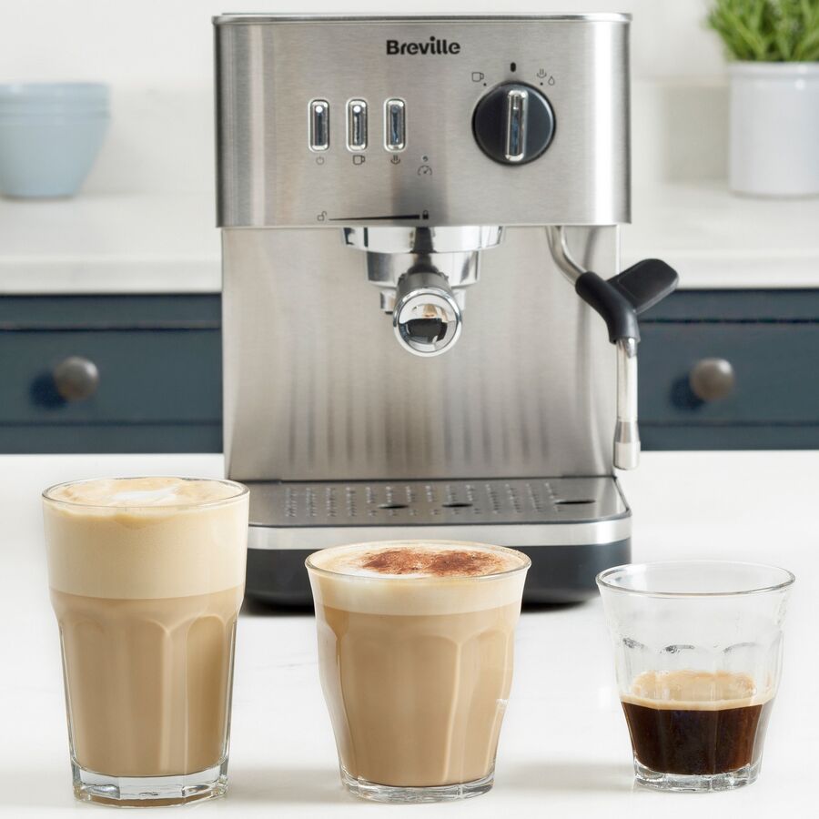 Espressomaskine i stål på en køkkenbordplade med latte, cappuccino og en espresso foran
