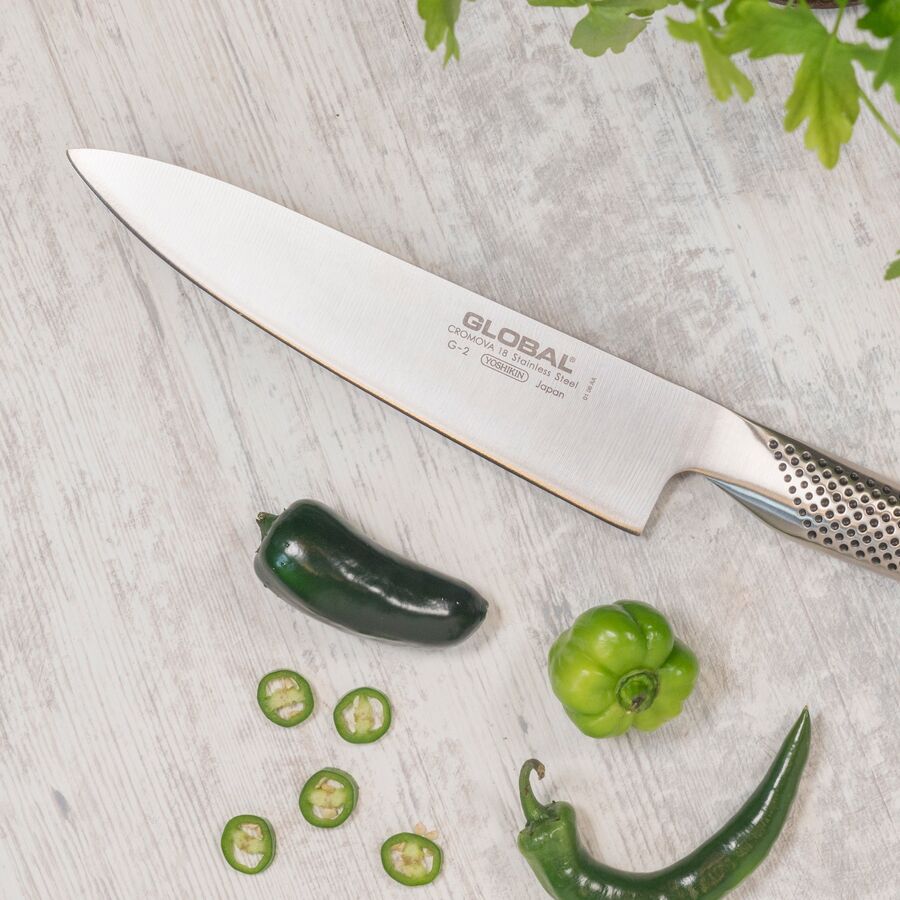 Global kokkekniv på en lys stenbordplade med hele og snittede jalapeños