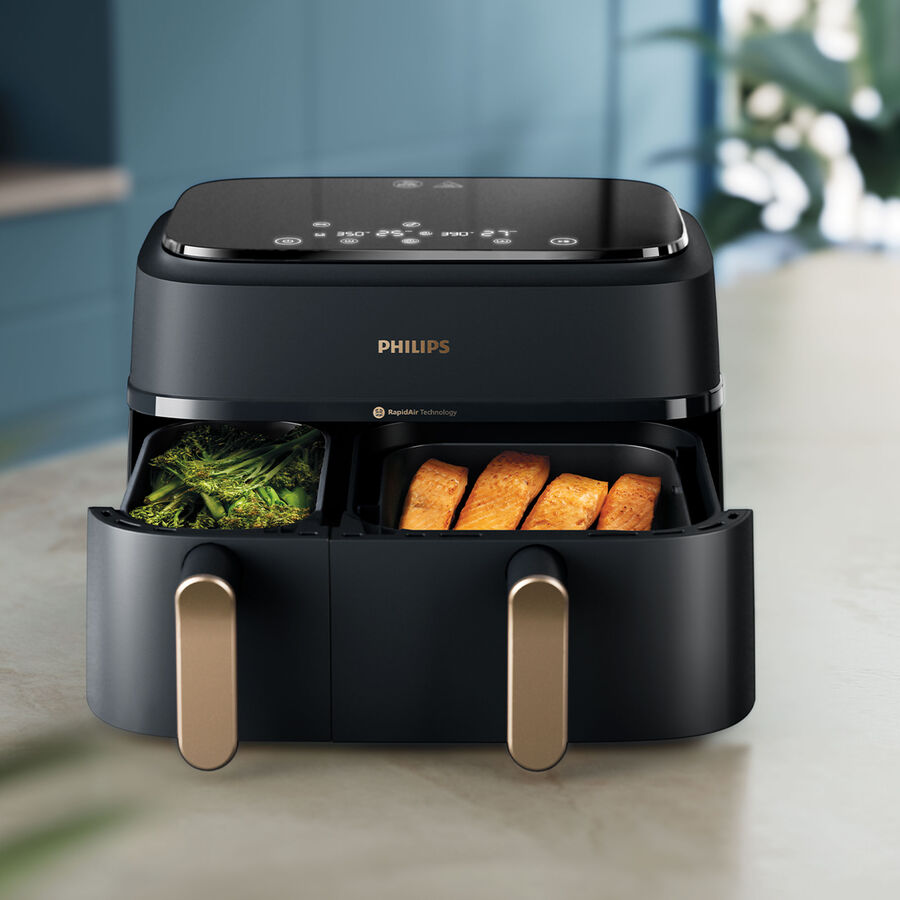 Sort airfryer med to skuffer trukket ud på en køkkenbordplade, grønne bønner i den ene og panerede stykker i den anden
