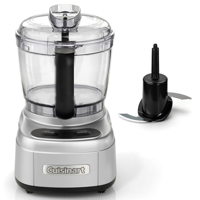 Lille foodprocessor på hvid bund med børstet stålsokkel, klar skål med sort midterakse og et sort kombinationsblad liggende ved siden af