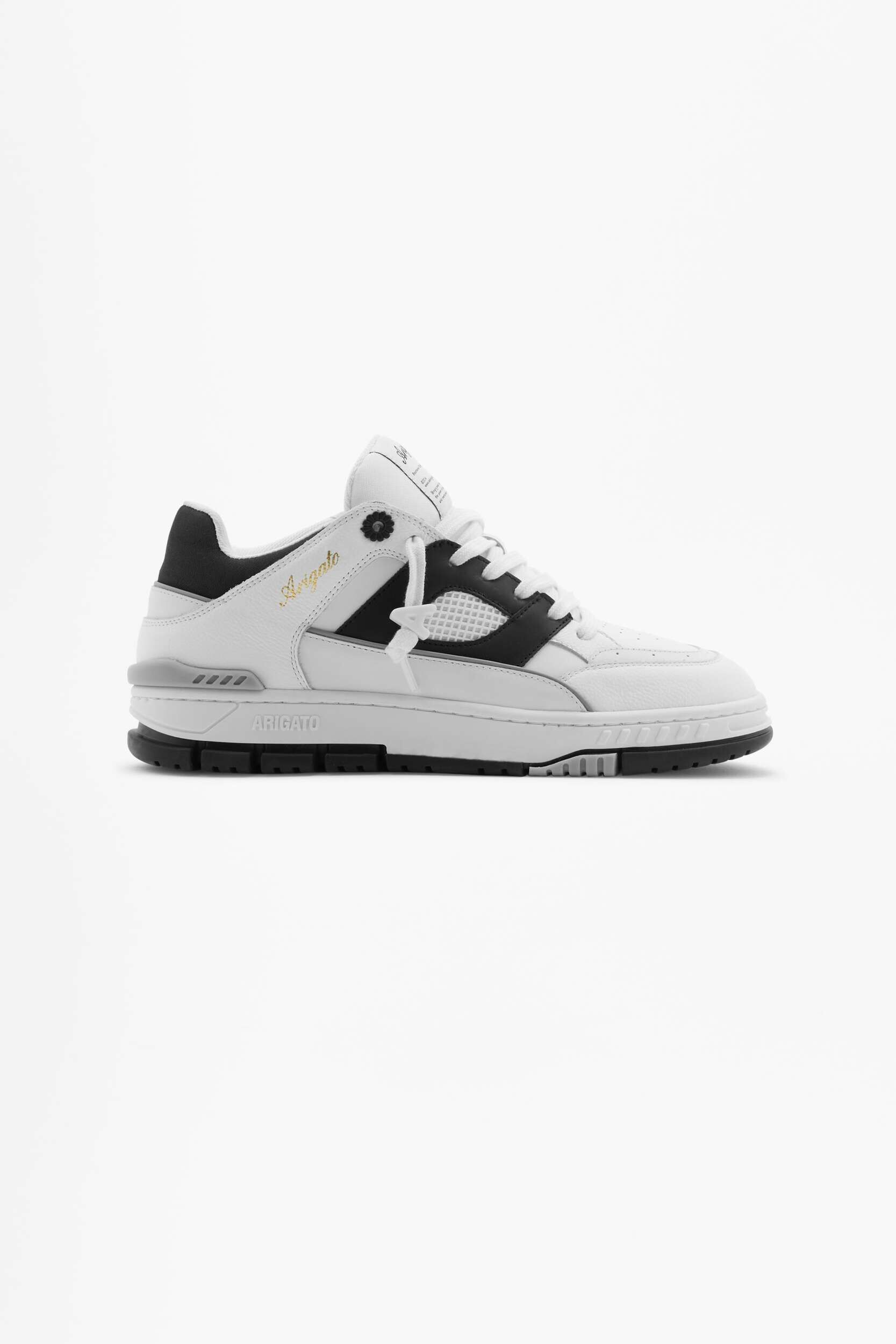 A white low-top sneaker with black accents and white laces, featuring 'Arigato' branding in gold script on the side and 'ARIGATO' in white text on the midsole, displayed against a plain white background.
