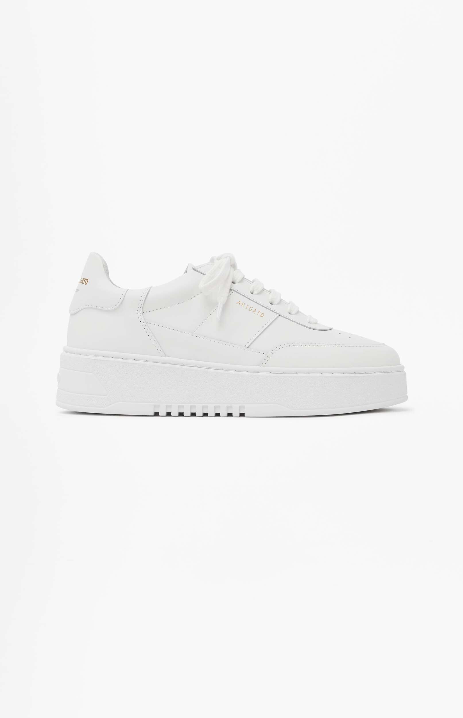 A pristine white Axel Arigato low-top sneaker with white laces and a thick white sole, shown on a plain white background. The brand name 'ARIGATO' is subtly visible in gold lettering on the side.
