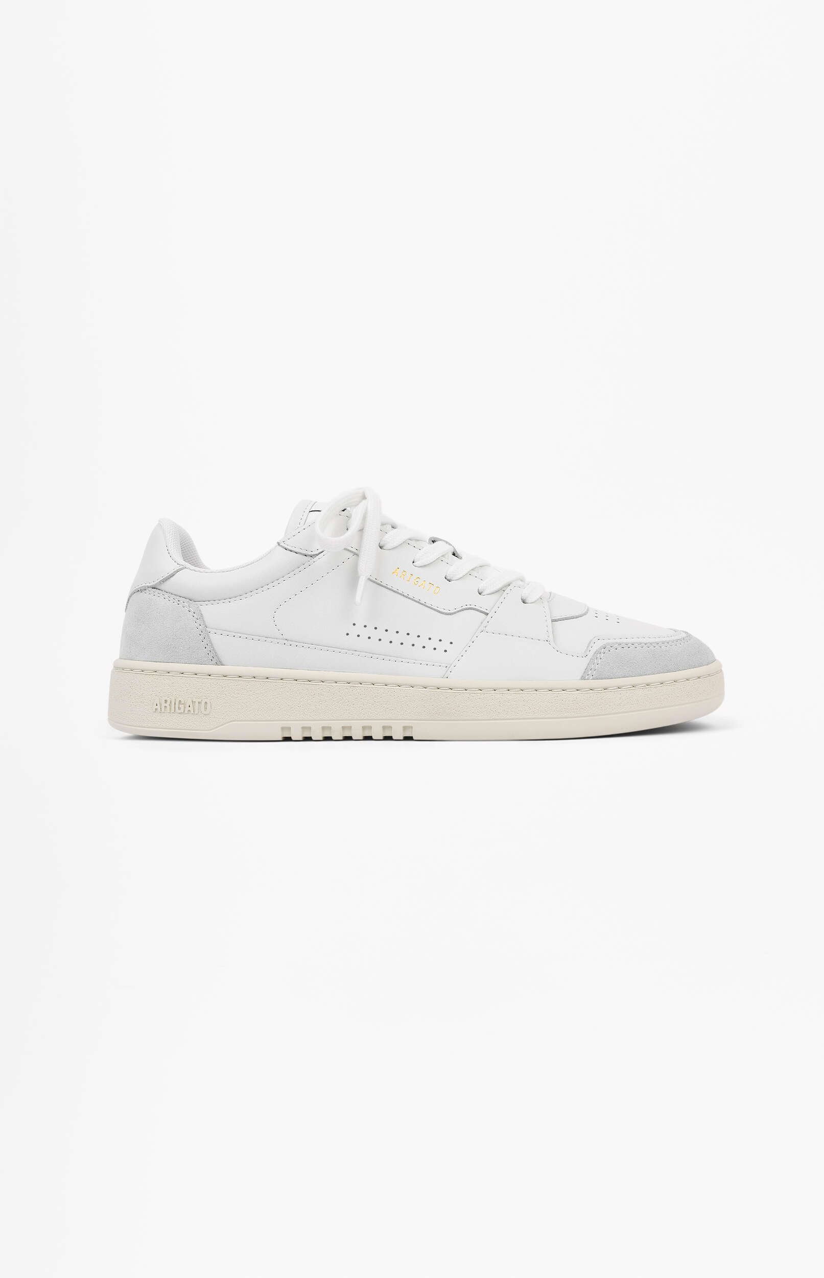 A clean white Axel Arigato low-top sneaker with light grey suede accents on the heel and toe, white laces, and a thick cream-colored sole. The brand name 'ARIGATO' is subtly visible in gold lettering on the side and embossed on the sole. The shoe is photographed against a bright white background.