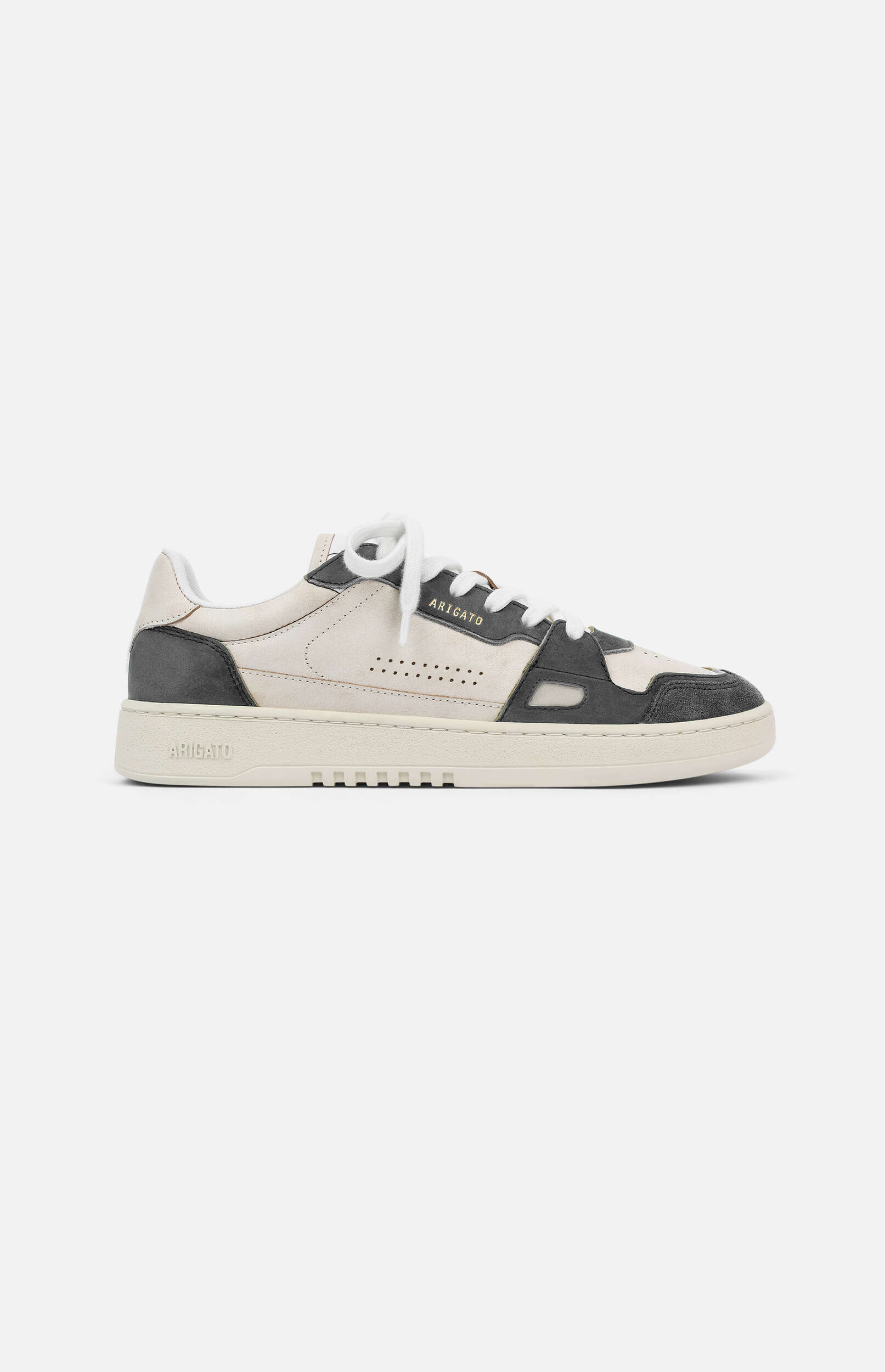 A single low-top sneaker from Axel Arigato, featuring an off-white main body with dark grey suede overlays on the toe, side, and heel. The sneaker has white laces and a thick, cream-colored sole with the 'ARIGATO' brand name subtly embossed on the side. The shoe is presented in a clean side profile against a plain, light grey background.