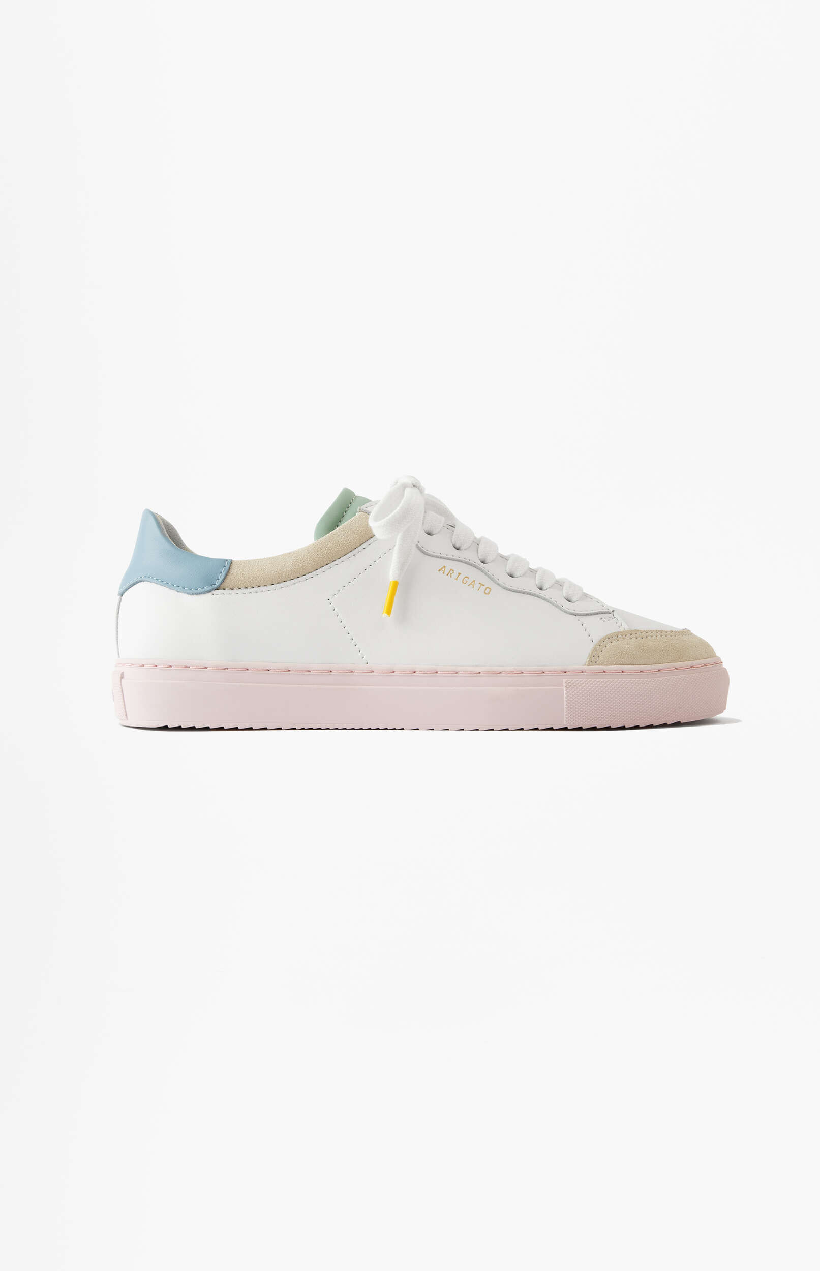 A white leather Axel Arigato sneaker with a light pink sole, light blue heel tab, light green ankle collar, and a beige suede toe cap. The white laces have a yellow aglet, and 'ARIGATO' is debossed on the side. The sneaker is shown in profile on a plain white background.