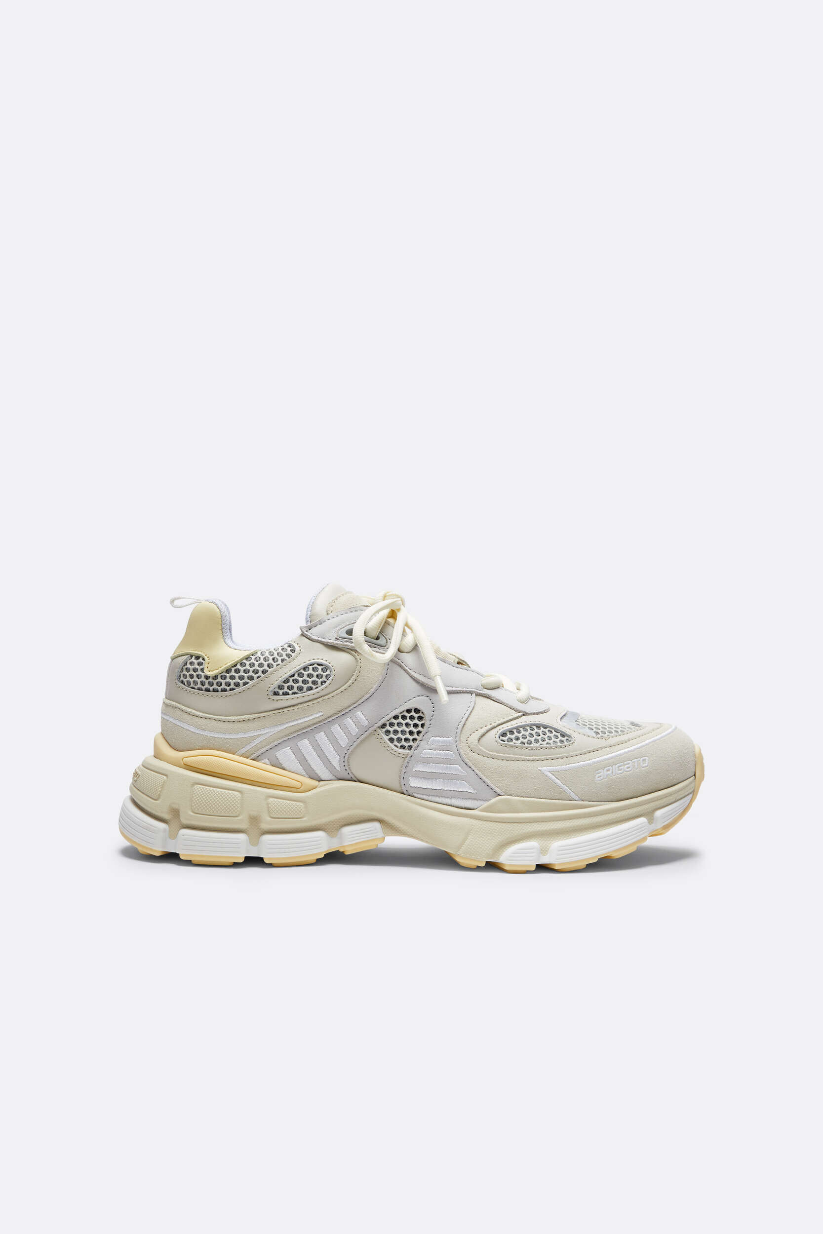 A light cream and beige Axel Arigato Genesis Vintage Runner sneaker, viewed from the side. The shoe features a mix of mesh, suede, and synthetic overlays, a chunky multi-layered sole with yellow accents, and white laces. The brand name 'ARIGATO' is subtly visible on the toe area.