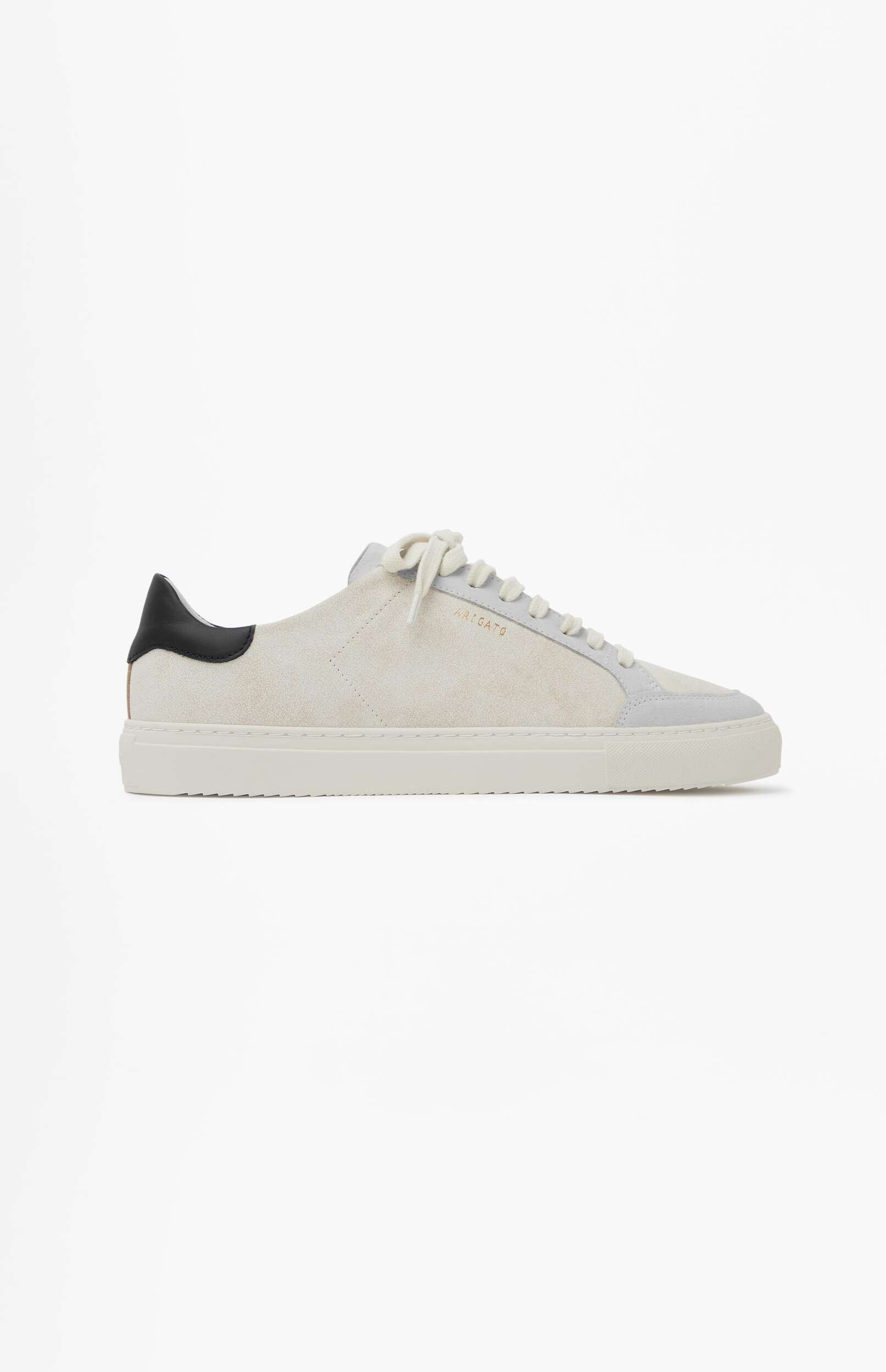 A white and light grey suede sneaker with a black heel tab, featuring white laces and a white rubber sole, shown from the side on a plain white background. The brand name 'ARIGATO' is visible in gold text on the side.