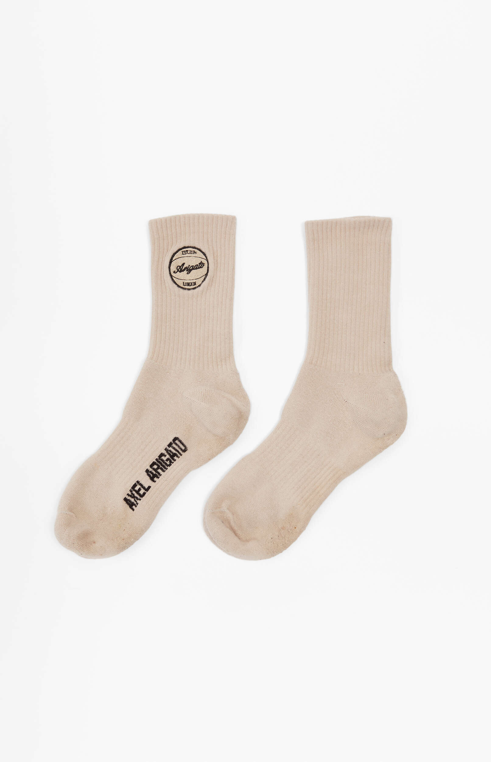 A pair of light beige ribbed crew socks laid flat on a white background. The left sock features a circular black logo with 'EST. 2014 Arigato LONDON' on the ankle and 'AXEL ARIGATO' printed in black along the arch/sole.