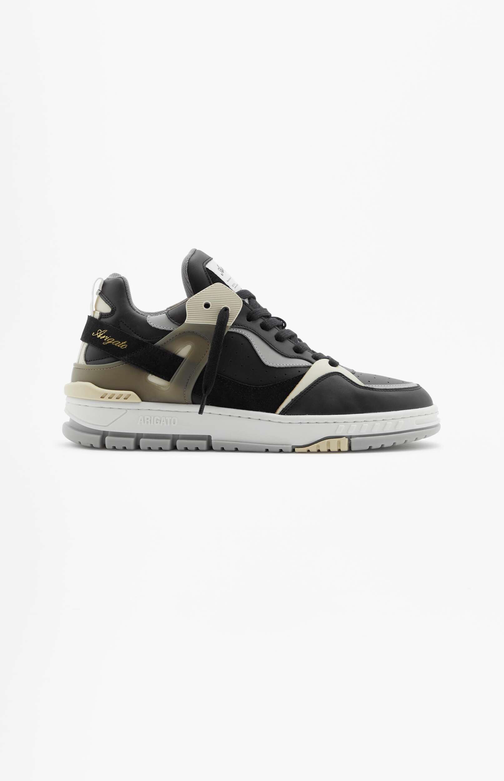 A black and white chunky sneaker with grey and light tan accents, featuring the 'Arigato' brand name in gold script on a heel strap, displayed against a clean white background.