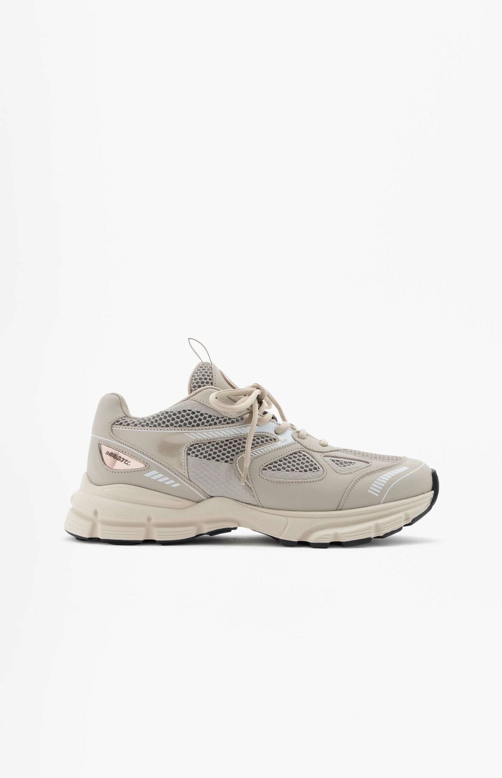 A light beige or tan chunky sole sneaker is displayed against a plain white background, viewed from the side. The shoe features mesh panels, synthetic overlays, and a thick sole with visible texture and a black outsole. There are subtle reflective details on the side.