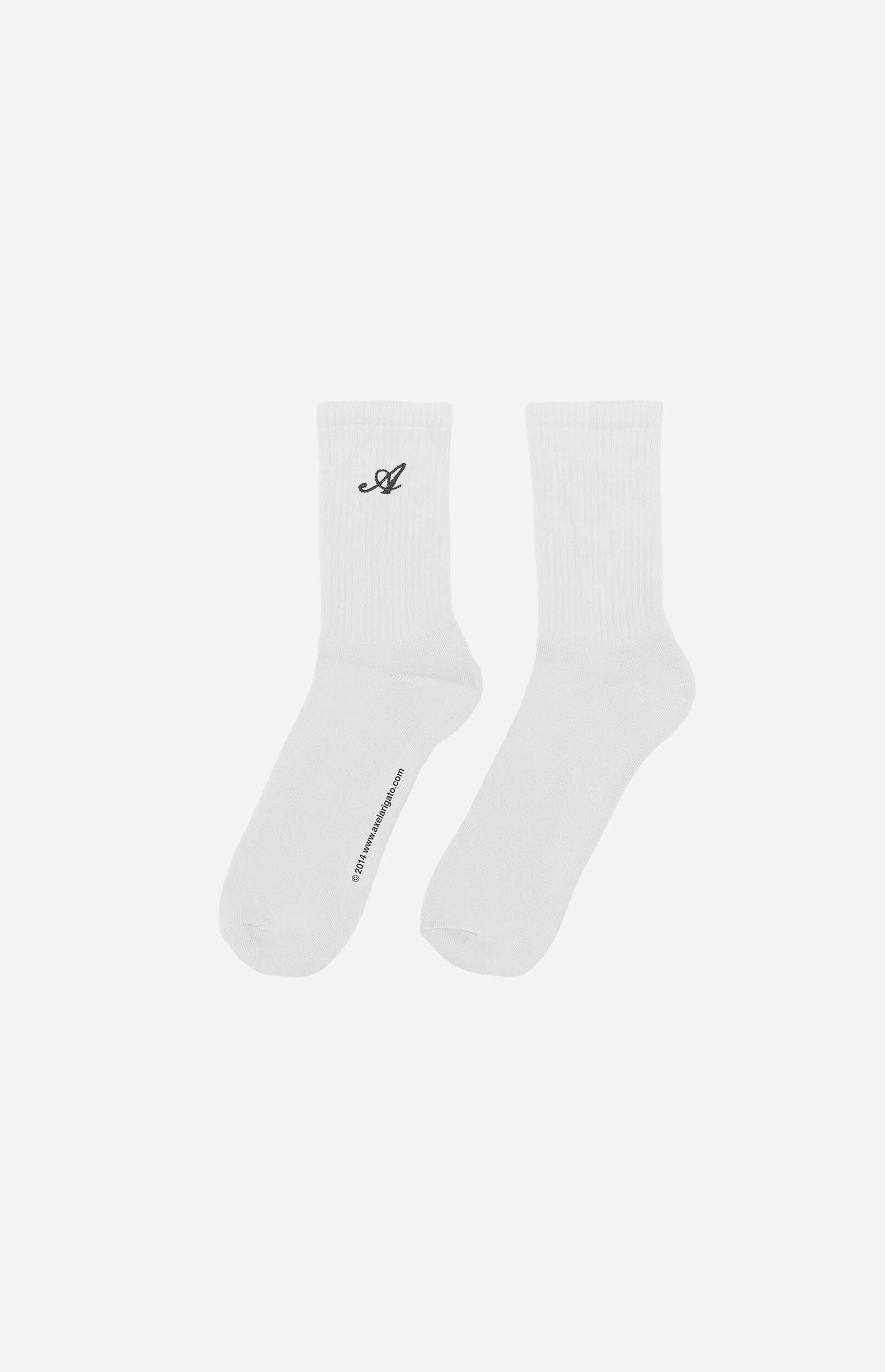 A pair of white crew socks are shown against a light grey background. The left sock has a black embroidered cursive 'A' logo near the cuff and the text '© 2014 www.axelarigato.com' printed vertically along the side of the foot. The right sock is plain white.