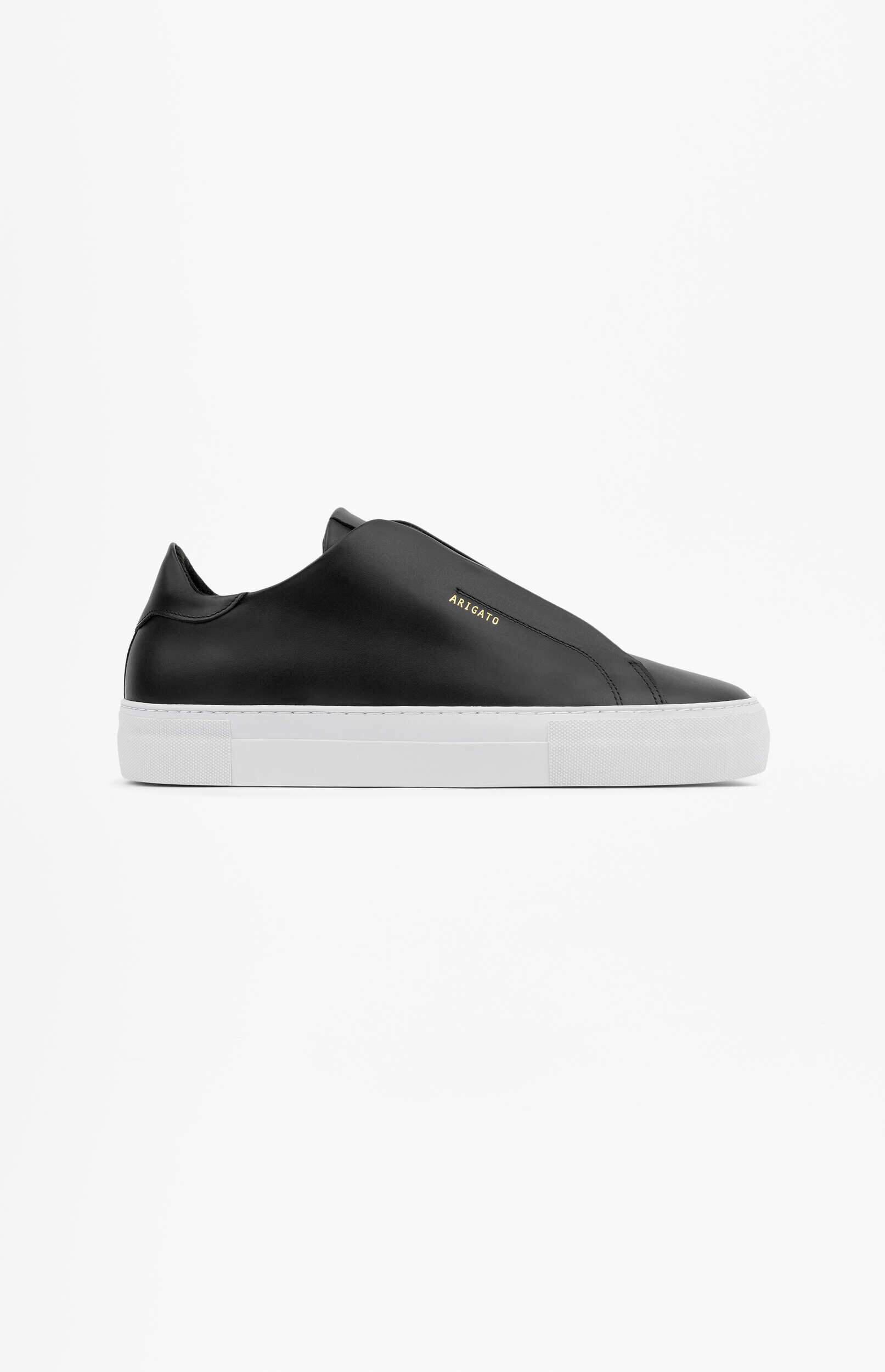 A black leather slip-on sneaker with a thick white sole is shown from a side profile on a plain white background. The brand name 'ARIGATO' is visible in gold text on the side of the shoe.