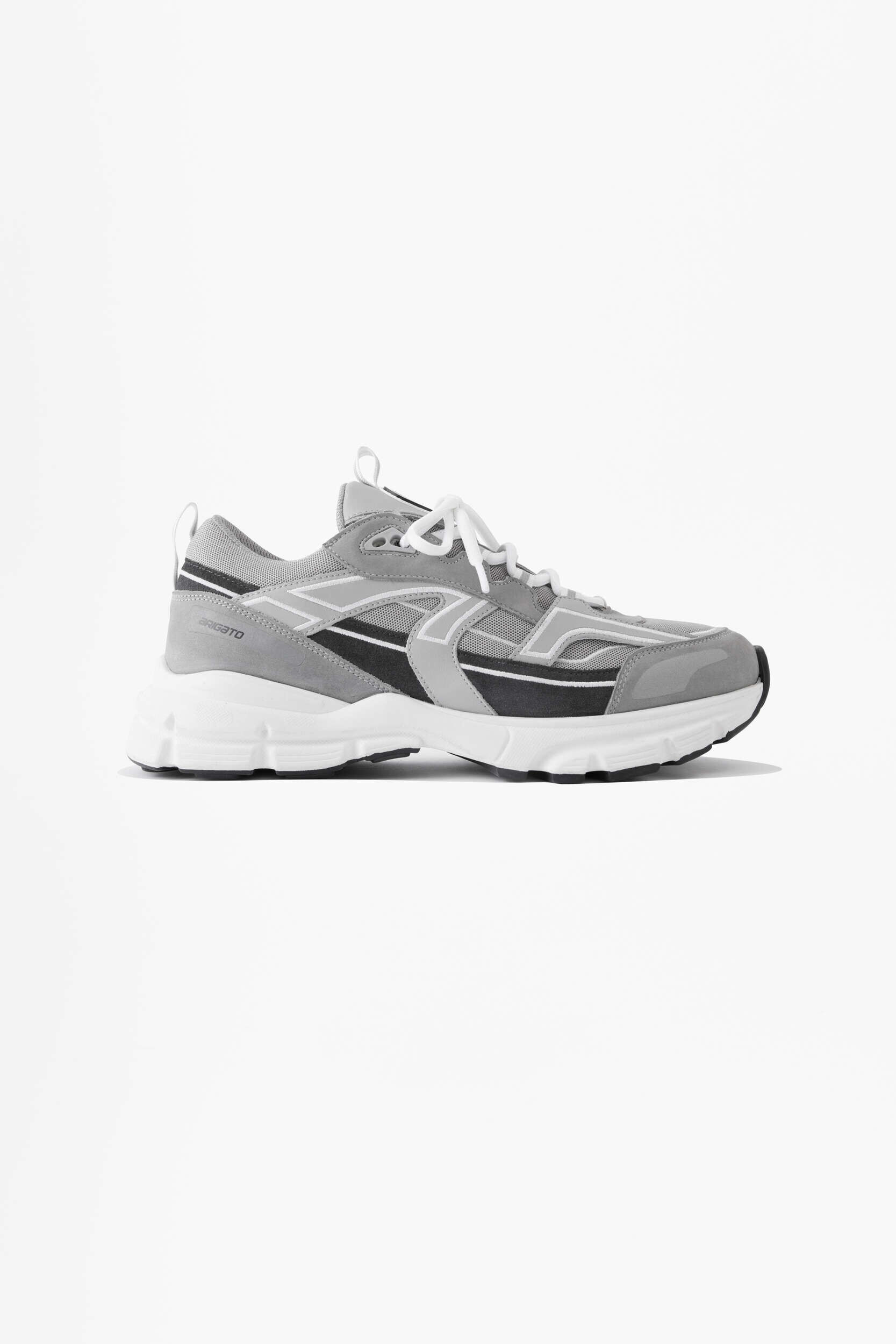 A single gray and black sneaker with white accents and laces, featuring a chunky white sole, viewed from the side on a white background. The brand name "BRIGATO" is visible near the heel.