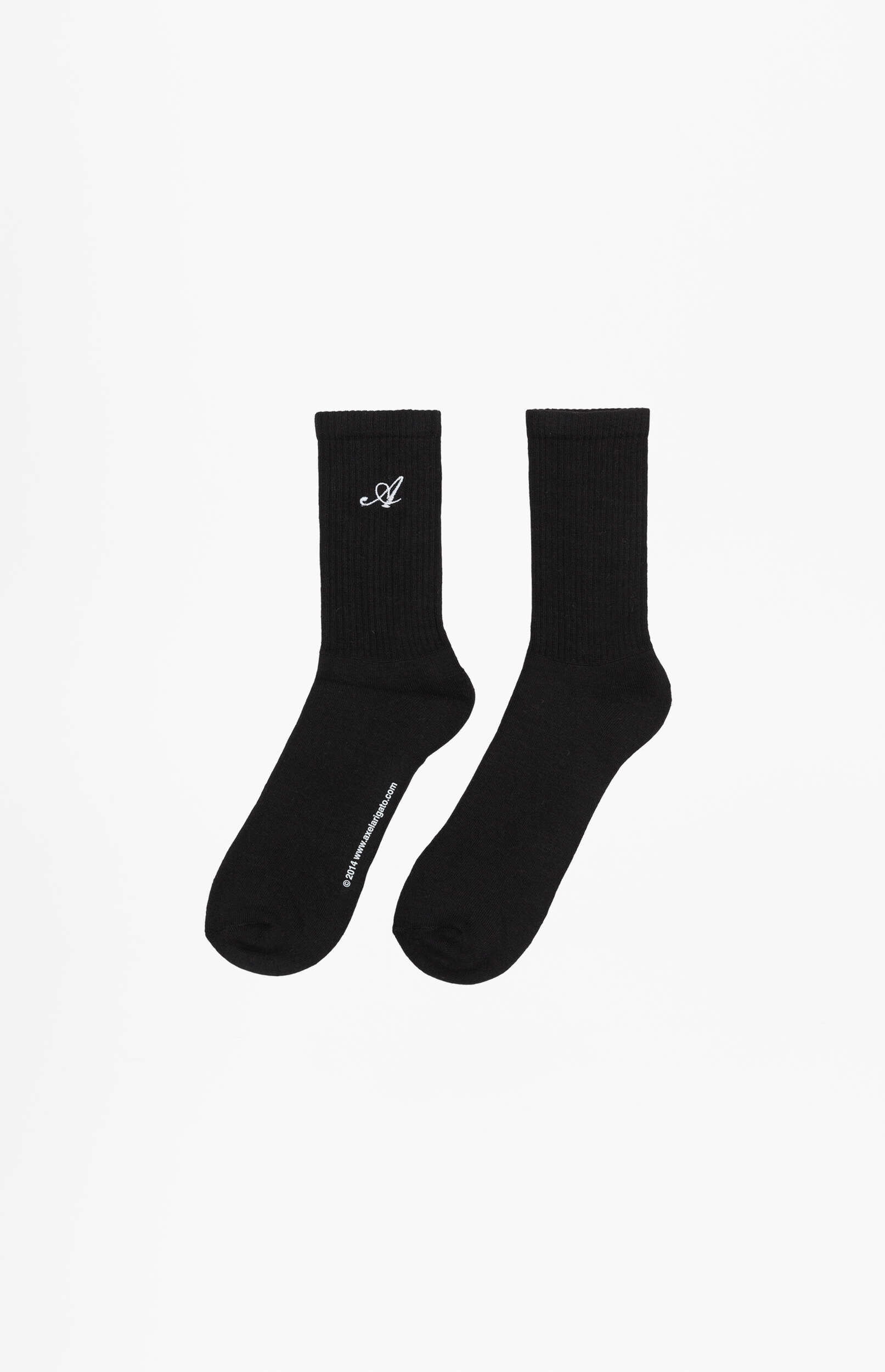 A pair of black crew socks with ribbed cuffs. The left sock features a small white embroidered cursive 'A' near the cuff and '© 2014 www.axelarigato.com' printed vertically on the side. The socks are displayed against a clean white background.