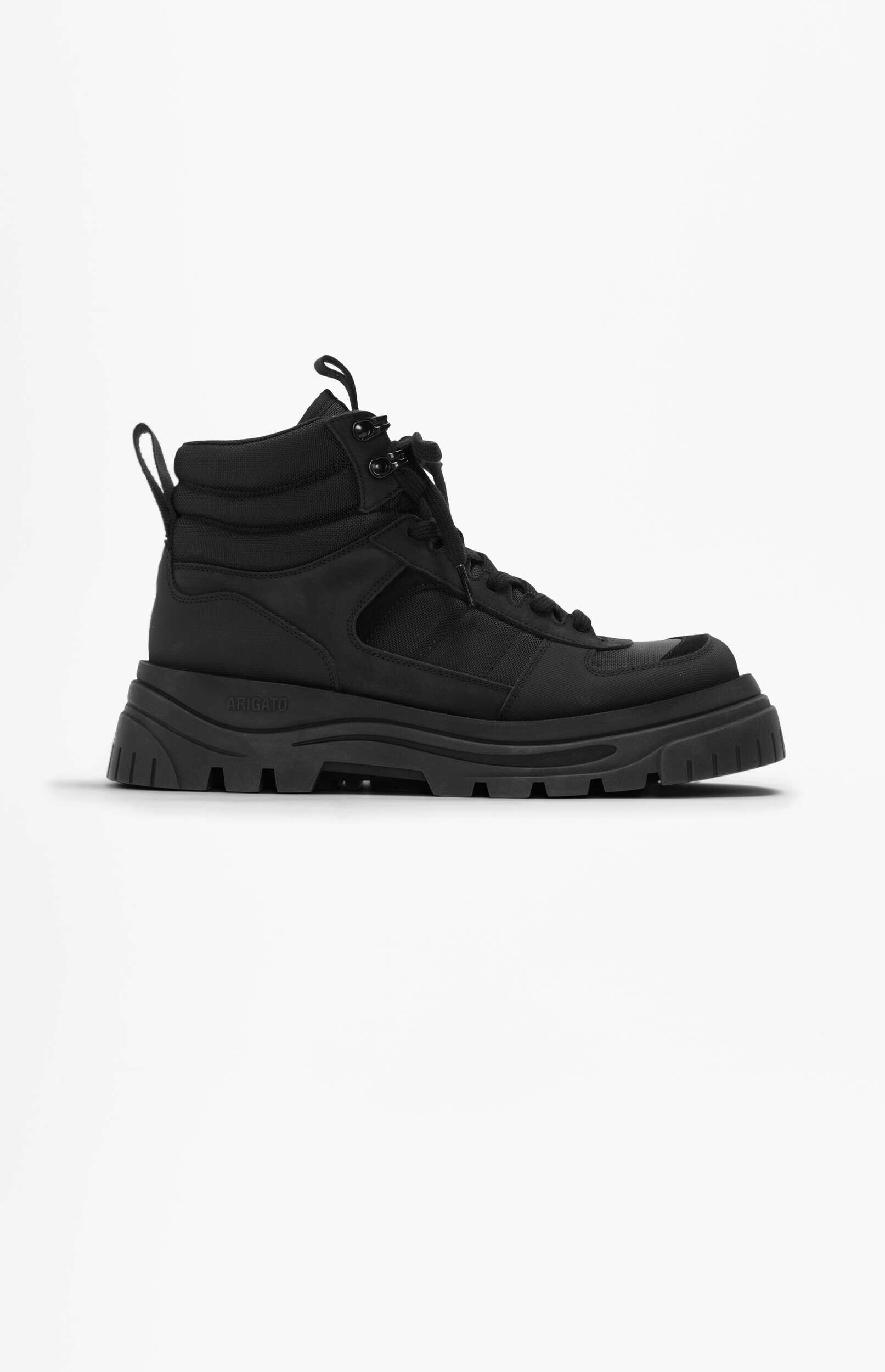 A single black high-top sneaker boot with a chunky, ridged sole is positioned against a clean white background. The boot features a matte black upper with visible stitching and textured panels, along with black laces and a heel pull tab. The word 'ARIGATO' is subtly embossed on the outer side of the thick sole.