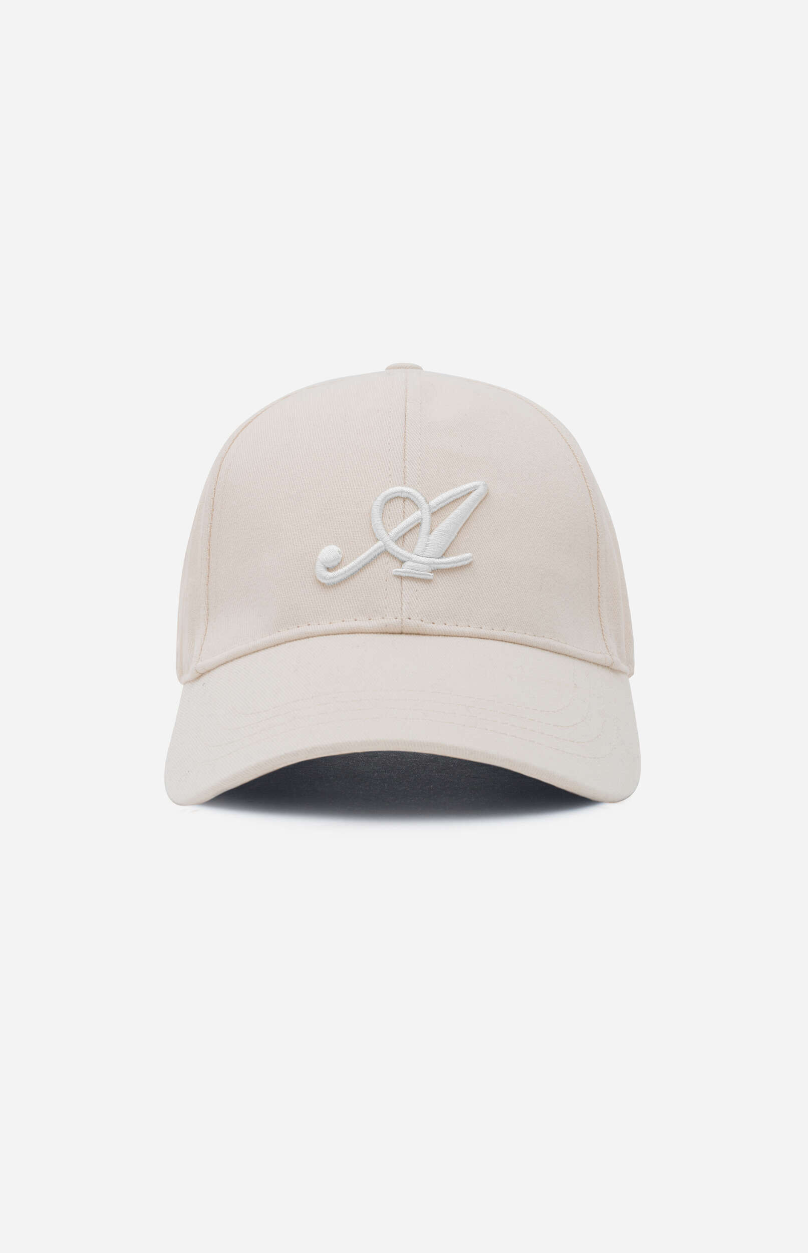 A light beige baseball cap is centered against a plain light gray background. The cap features a prominent white embroidered, stylized letter 'A' on the front panel. The brim is curved.