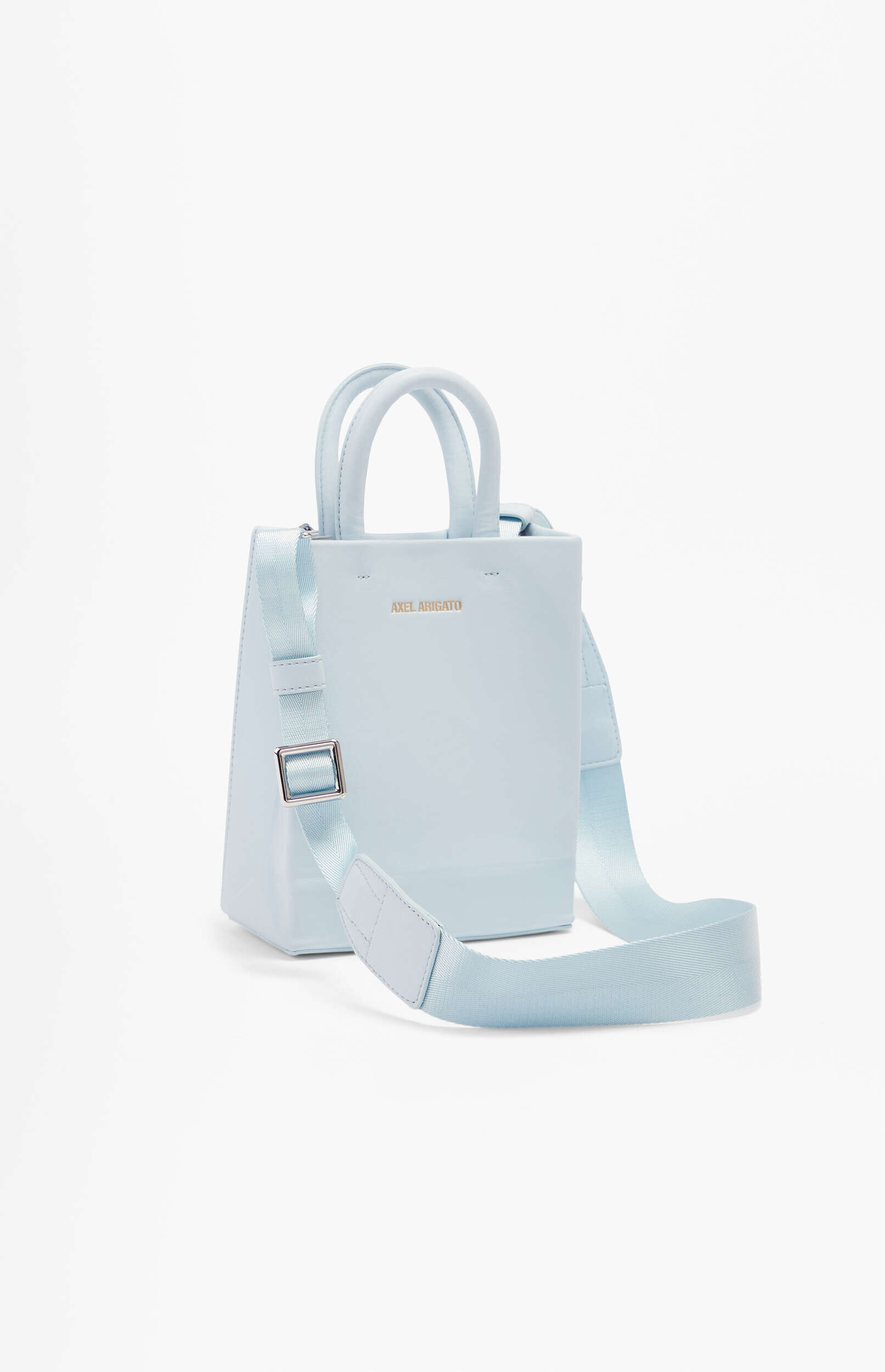 A light blue Axel Arigato mini tote bag with dual top handles and a wide, adjustable shoulder strap. The bag has a rectangular shape and is made of smooth material, with the 'AXEL ARIGATO' logo embossed in metallic gold on the front. It is displayed on a plain white background.