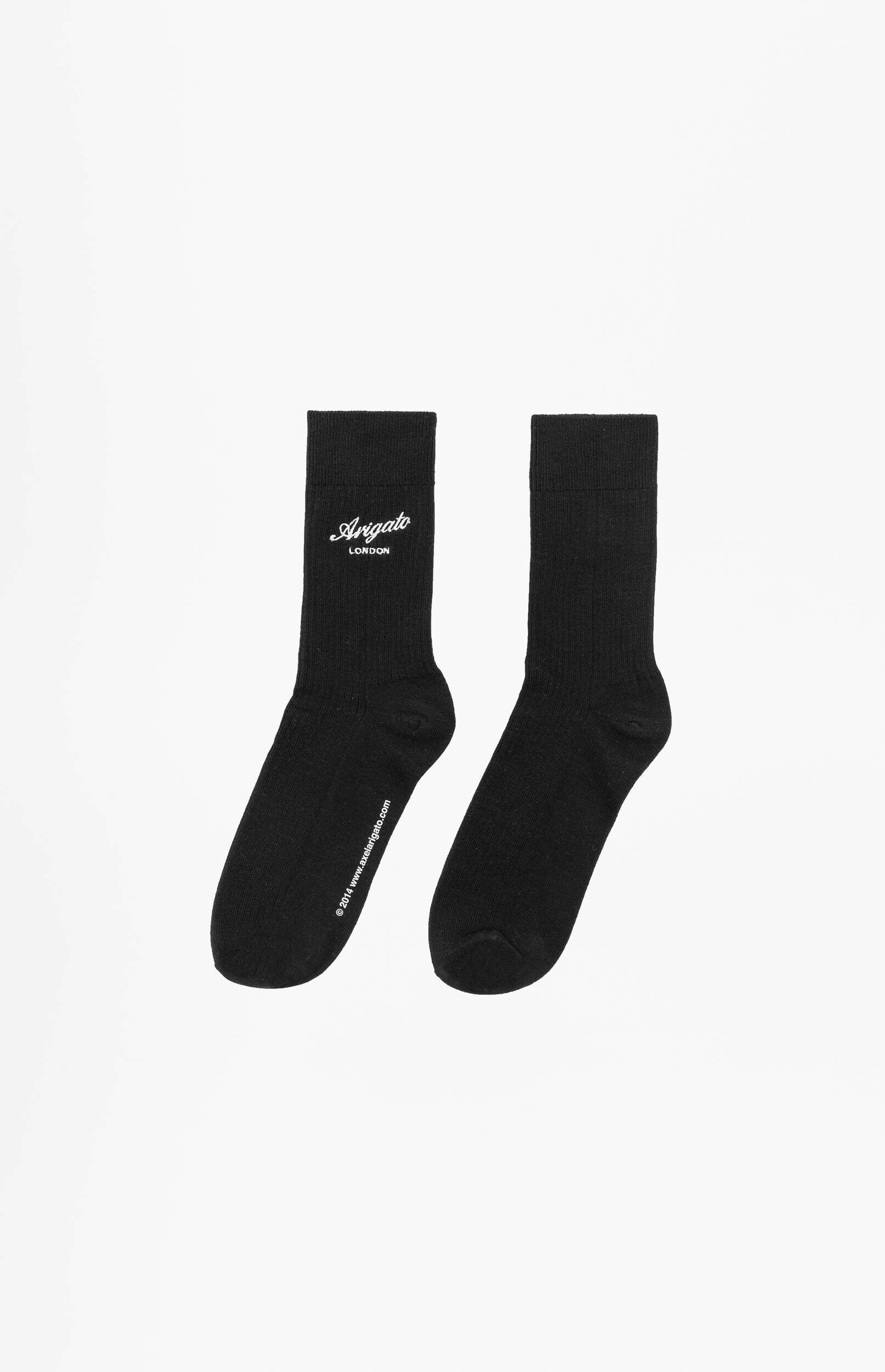 A pair of black crew socks displayed on a white background. The left sock features a white 'Arigato London' logo on its cuff, while the right sock is plain black. Both socks also have a small '© 2014 www.axelarigato.com' text along the foot area.