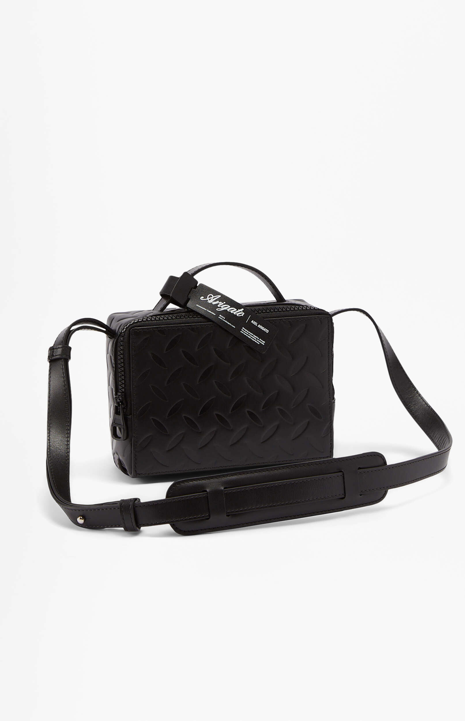 A black leather Axel Arigato cross-body bag with an embossed diamond plate pattern. The bag features a top zipper closure, a structured rectangular shape, and an adjustable shoulder strap with a padded section. A black brand tag with 'Arigato' and 'AXEL ARIGATO' is attached to the top handle. The bag is positioned at an angle on a plain white background.