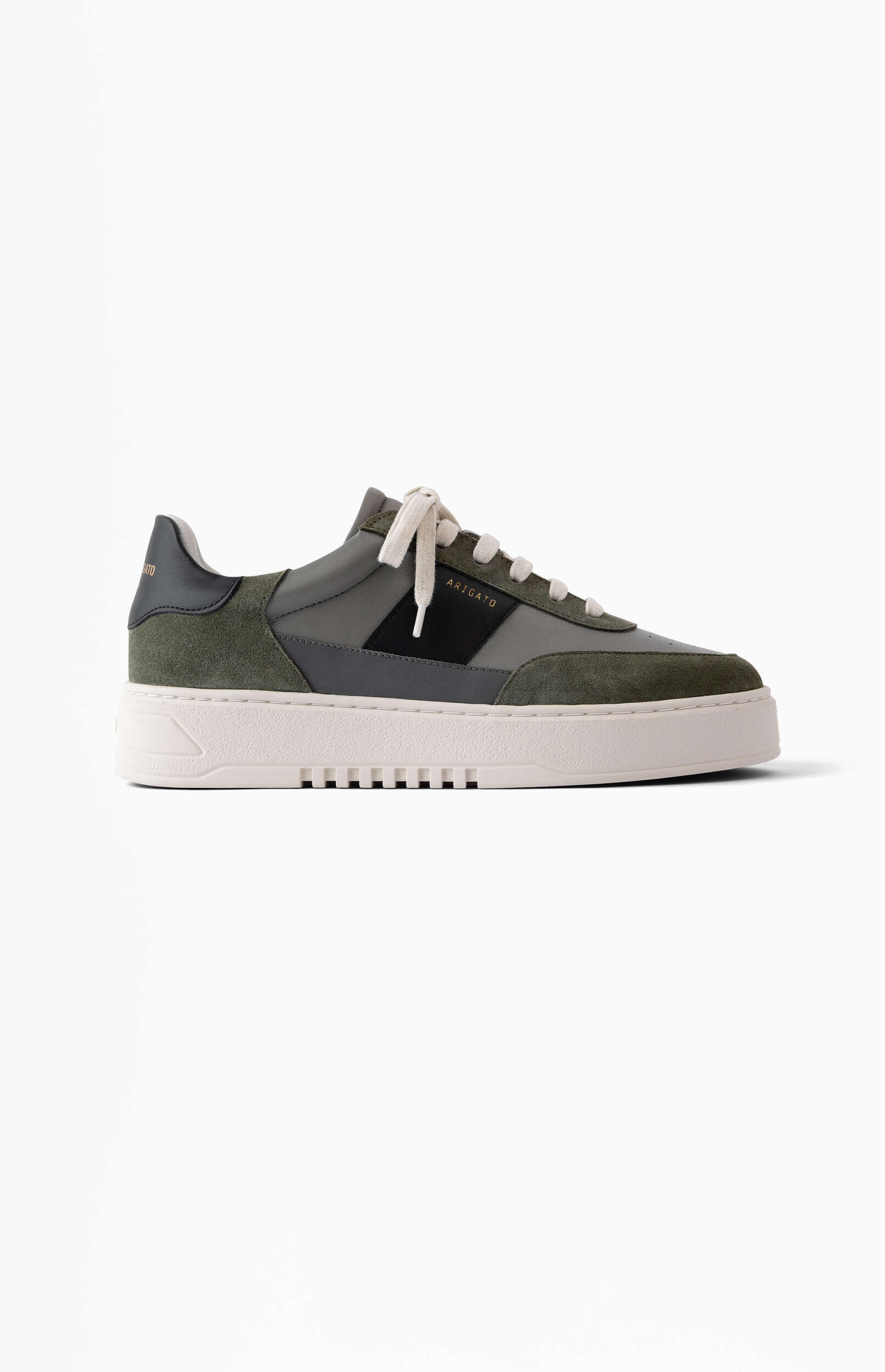 A single Axel Arigato low-top sneaker displayed from the side. The shoe features olive green suede and dark grey leather panels, with a black stripe on the side bearing the 'ARIGATO' logo in gold text. It has off-white laces and a thick, off-white textured sole. The background is solid white.