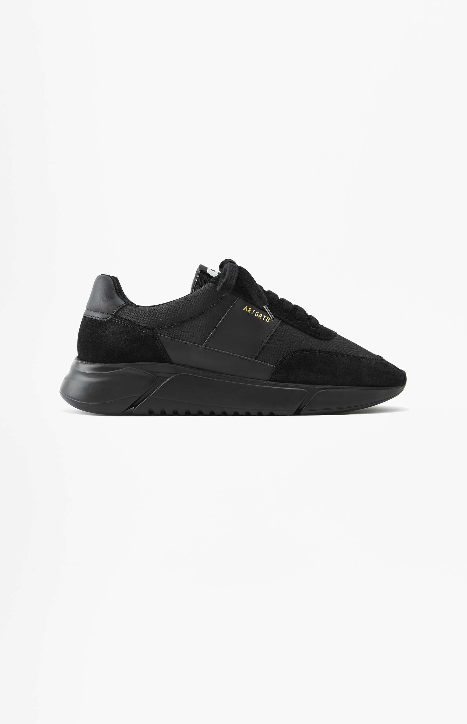 A single black Axel Arigato Genesis sneaker, featuring a chunky black sole and a mixed-material upper with suede and matte panels. The brand name 'ARIGATO' is visible in gold lettering on the side of the shoe. The sneaker is presented against a clean white background, viewed from a side profile.